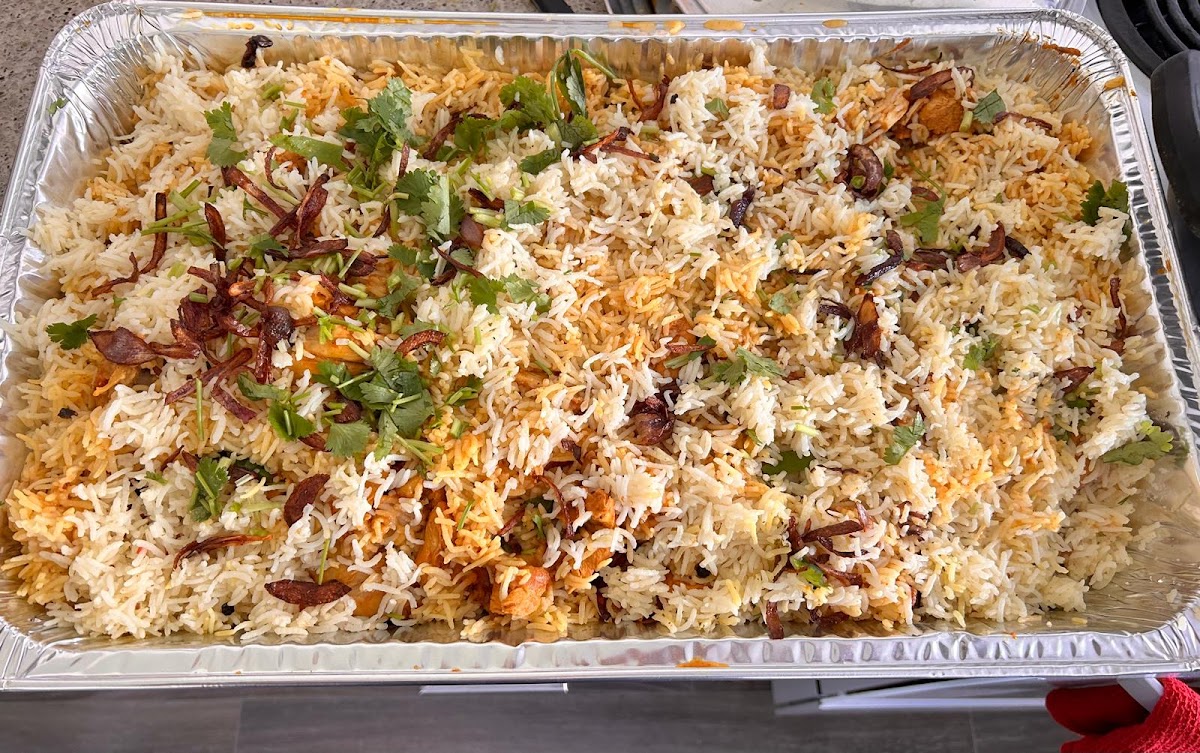 A full catering tray of chicken biryani topped with fried onion and coriander